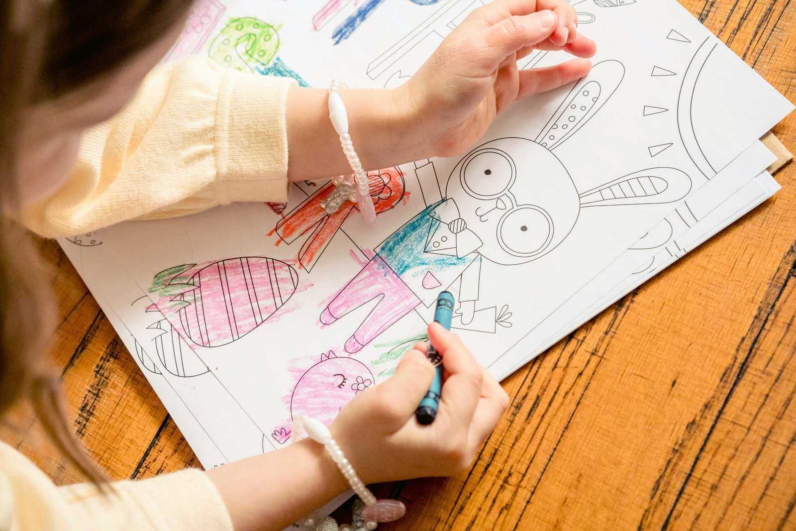 From above of crop unrecognizable girl in casual clothes drawing in coloring book in daylight